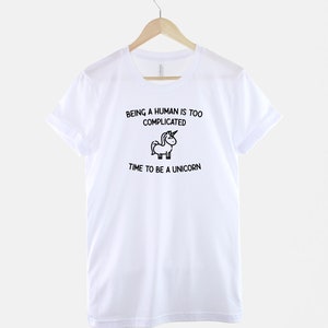 May include: White t-shirt with black text that reads "Being a human is too complicated. Time to be a unicorn." A small black and white unicorn illustration is between the two lines of text.