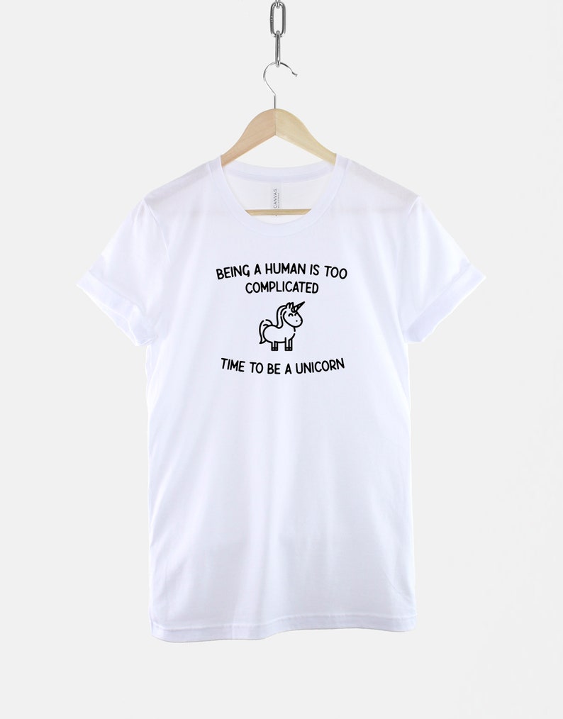 May include: White t-shirt with black text that reads "Being a human is too complicated. Time to be a unicorn." A small black and white unicorn illustration is between the two lines of text.