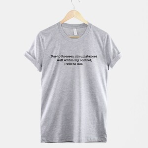 Op de afbeelding: Een grijs t-shirt met de tekst "Due to foreseen circumstances well within my control, I will be late."