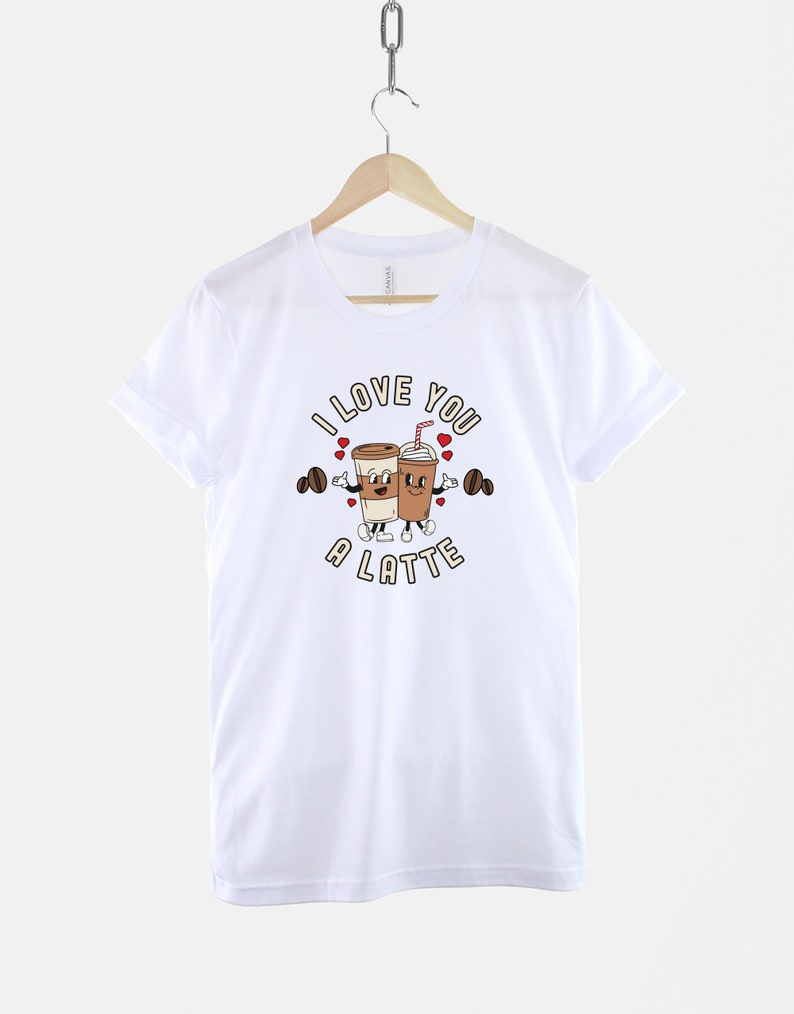 K&ouml;nnte beinhalten: Wei&szlig;es T-Shirt mit einem Motiv von zwei Kaffeetassen, die Hanteln halten, und dem Text "I love you a latte".