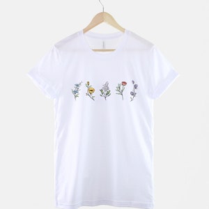 May include: White t-shirt with a line of five different coloured flowers printed on the front.