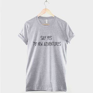 May include: Gray t-shirt with the text "Say yes to new adventures" printed on the front.