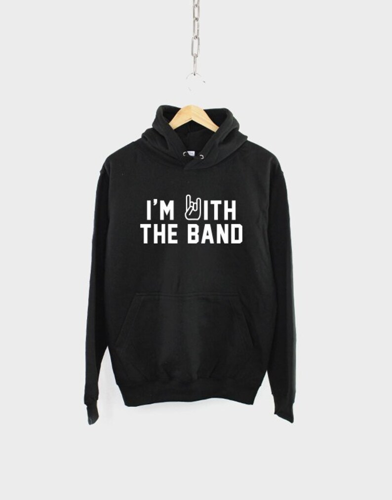 Puede incluir: Sudadera con capucha negra con texto blanco que dice "I'm with the band" y un gesto de mano de rock and roll.
