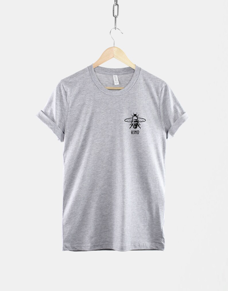 Op de afbeelding: Een grijs t-shirt met een zwarte bij-afbeelding en het woord "KIND" eronder.