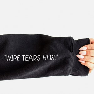 May include: Black sweatshirt with the text "WIPE TEARS HERE" printed in white on the sleeve.