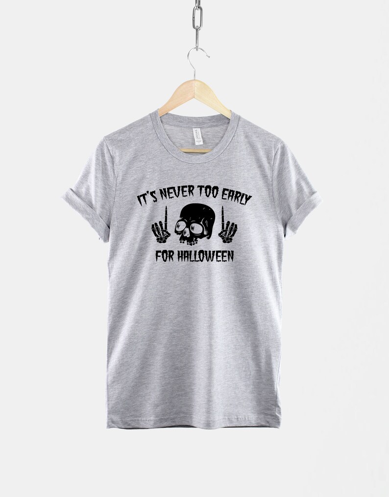 Peut inclure: T-shirt gris avec un motif de cr&acirc;ne et d'os crois&eacute;s noirs. Le texte "It's never too early for Halloween" est imprim&eacute; sous le cr&acirc;ne.