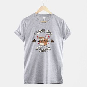 K&ouml;nnte beinhalten: Ein graues T-Shirt mit einem Motiv von zwei Kaffeetassen, die sich die H&auml;nde halten, und dem Text "I love you a latte".