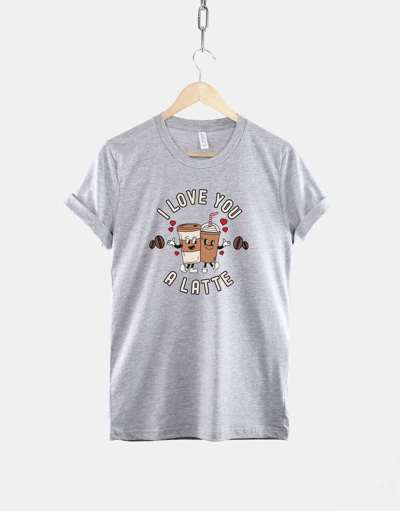 K&ouml;nnte beinhalten: Ein graues T-Shirt mit einem Motiv von zwei Kaffeetassen, die sich die H&auml;nde halten, und dem Text "I love you a latte".