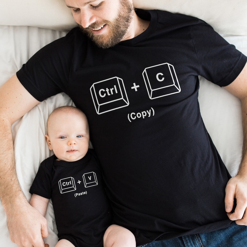 May include: A black t-shirt with the text "Ctrl + C (Copy)" on it. A baby is wearing a black onesie with the text "Ctrl + V (Paste)" on it.