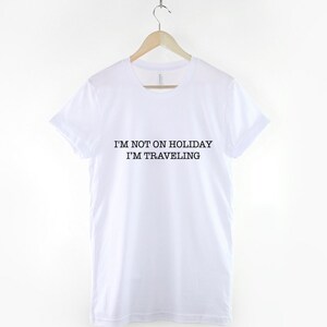 May include: White t-shirt with black text that reads "I'm not on holiday I'm traveling".