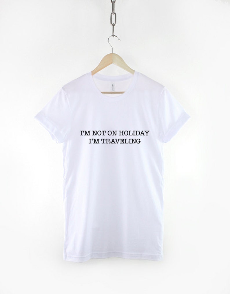 May include: White t-shirt with black text that reads "I'm not on holiday I'm traveling".
