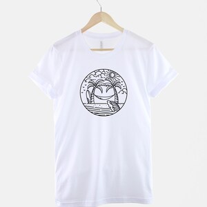 May include: White t-shirt with a black and white illustration of palm trees, a hammock, a surfboard, and a sun on a beach.