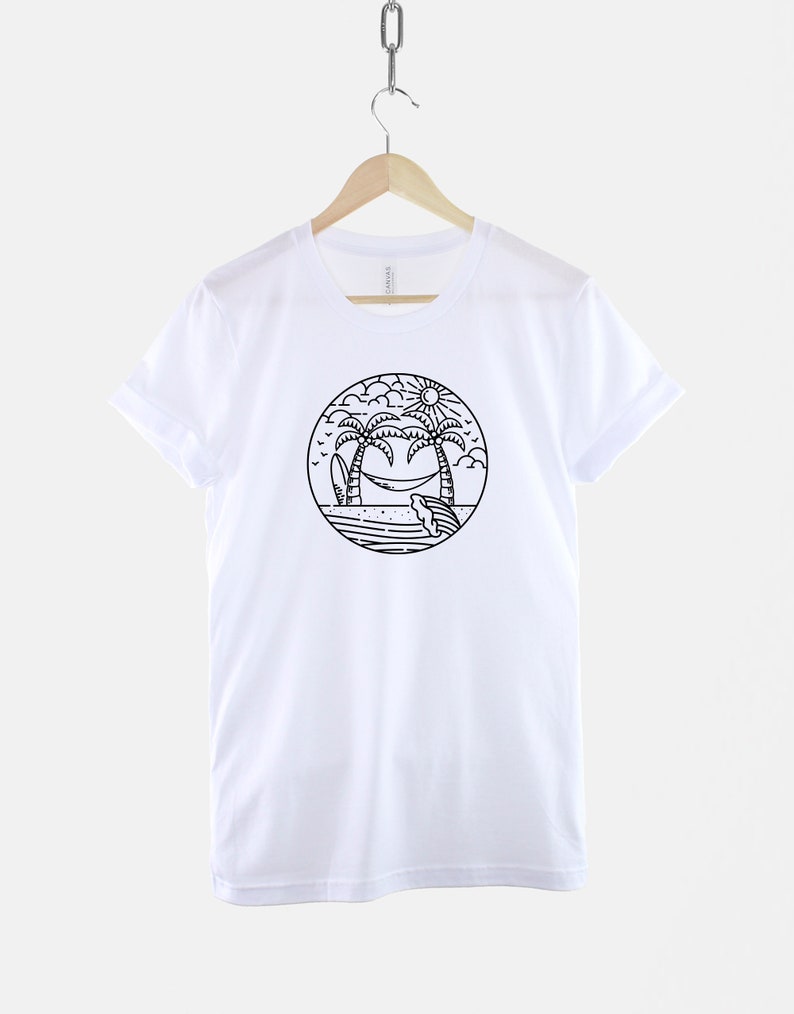 May include: White t-shirt with a black and white illustration of palm trees, a hammock, a surfboard, and a sun on a beach.