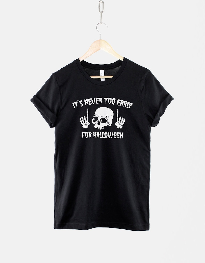 Peut inclure: T-shirt noir avec un motif de cr&acirc;ne et d'os crois&eacute;s blancs. Le texte "It's never too early for Halloween" est imprim&eacute; sur le t-shirt.