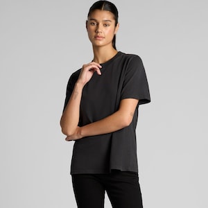 A woman wearing a black t-shirt stands with her arms crossed, looking directly at the camera.