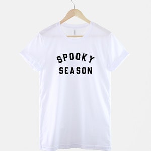 Puede incluir: Camiseta blanca con texto negro que dice "Spooky Season" en una percha.