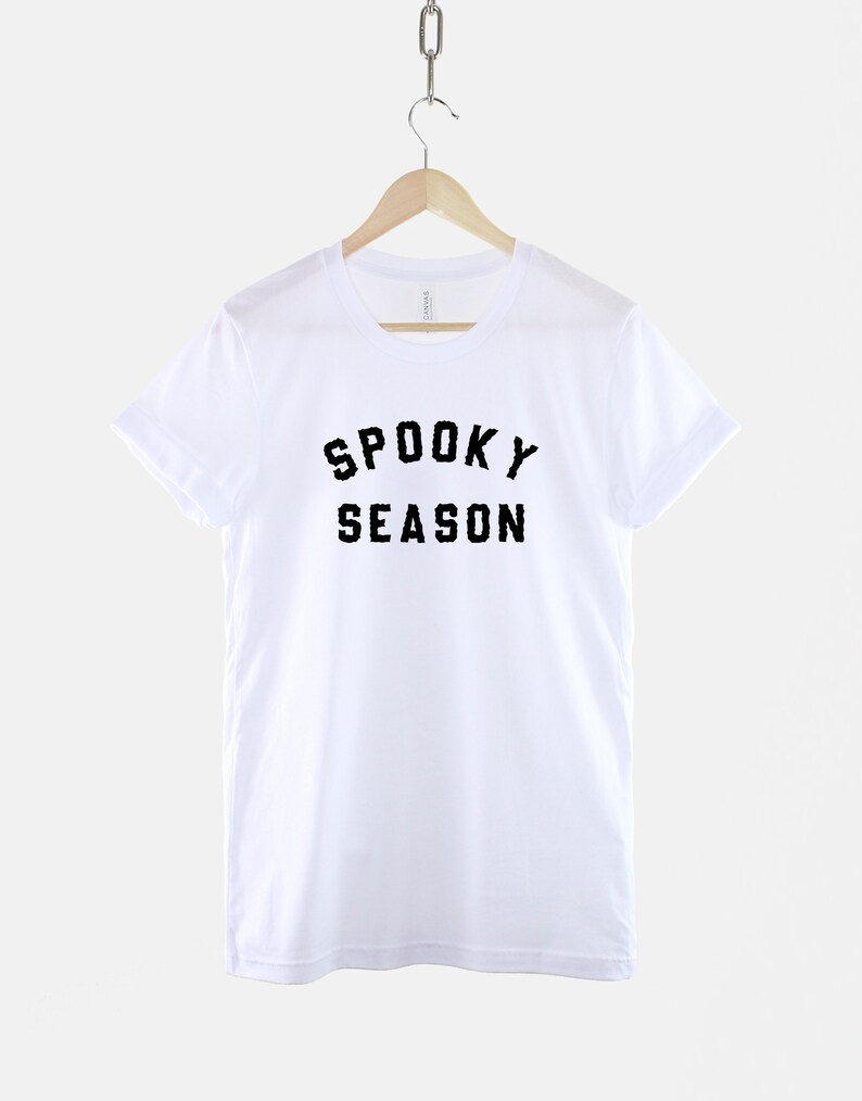 Puede incluir: Camiseta blanca con texto negro que dice "Spooky Season" en una percha.