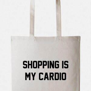 May include: A white canvas tote bag with black text that reads "SHOPPING IS MY CARDIO".