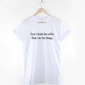 May include: White t-shirt with black text that reads "First I drink the coffee then I do the things."