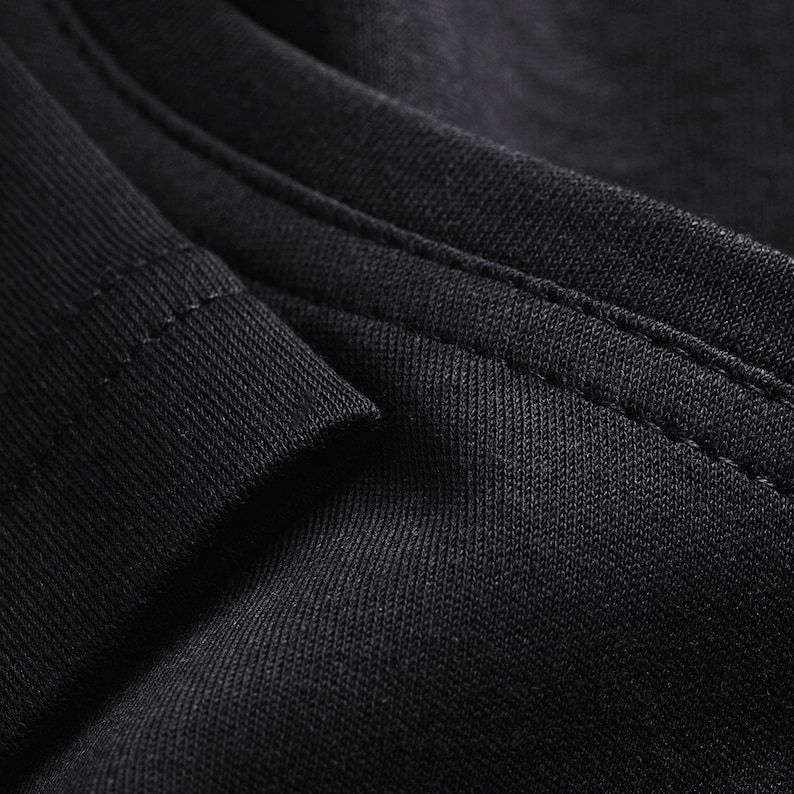 May include: Close-up of black fabric with a stitched seam. The fabric has a textured, woven appearance.