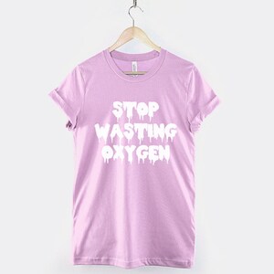 May include: A light pink t-shirt with the text "STOP WASTING OXYGEN" in white dripping letters.