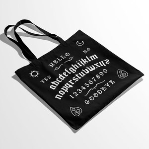 May include: Black canvas tote bag with a white ouija board design. The design includes the letters of the alphabet, numbers 1-0, and the words "YES", "NO", "HELLO", and "GOODBYE".