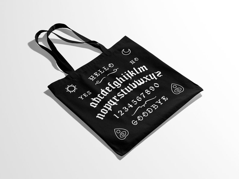 May include: Black canvas tote bag with a white ouija board design. The design includes the letters of the alphabet, numbers 1-0, and the words "YES", "NO", "HELLO", and "GOODBYE".