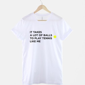 Op de afbeelding: Wit T-shirt met zwarte tekst die luidt "Het kost veel ballen om tennis te spelen zoals ik" en een gele tennisbal afbeelding.