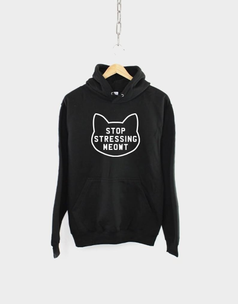 K&ouml;nnte beinhalten: Schwarzer Kapuzenpullover mit einem wei&szlig;en Katzenumriss und dem Text "STOP STRESSING MEOWT" auf der Vorderseite.