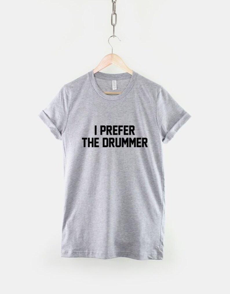 Puede incluir: Una camiseta gris con el texto "I prefer the drummer" impreso en negro.