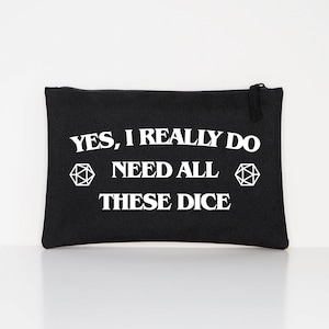 Puede incluir: Bolsa rectangular negra con cierre de cremallera. Texto blanco en la parte delantera que dice "YES, I REALLY DO NEED ALL THESE DICE", con dos formas geom&eacute;tricas blancas. La bolsa es de tela.