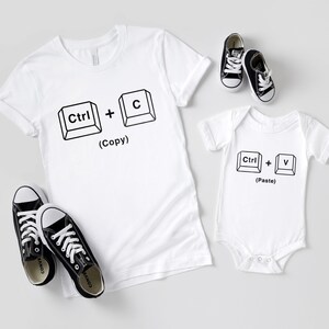 May include: White t-shirt with the text "Ctrl + C (Copy)" and a white onesie with the text "Ctrl + V (Paste)".