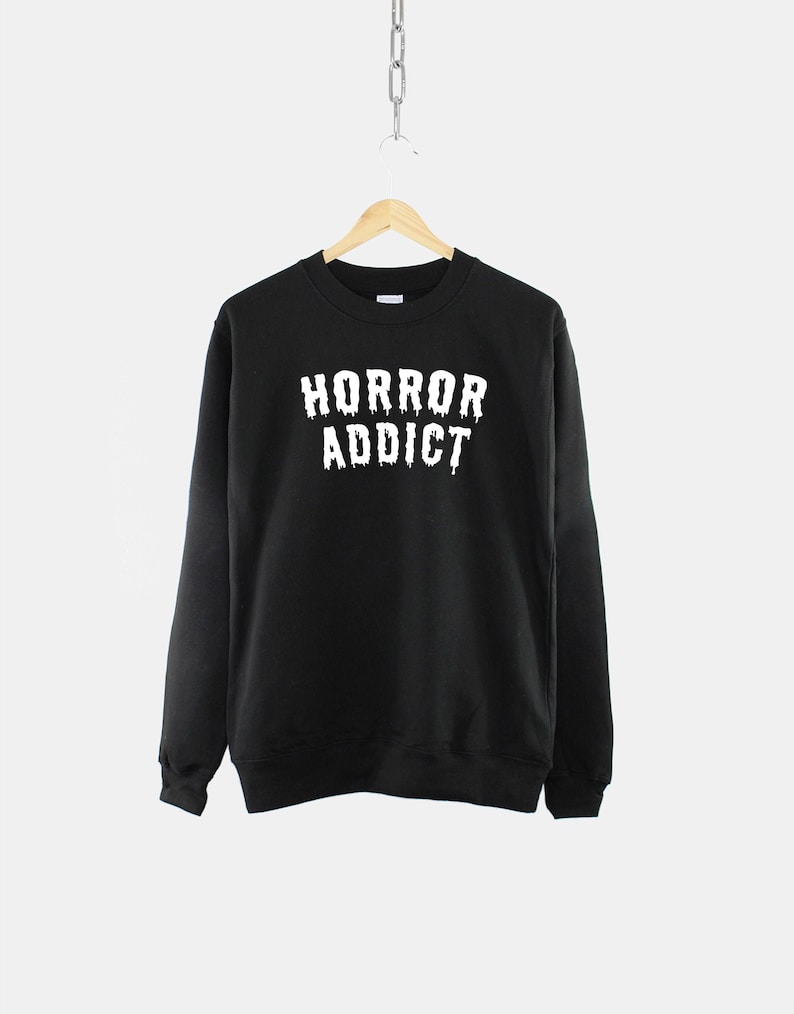 Puede incluir: Sudadera negra con texto blanco que dice "HORROR ADDICT" en letras que gotean.