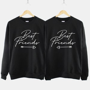 Może przedstawiać: Dwie czarne bluzy z białym napisem "Best Friends" z grafiką strzałki i serca.