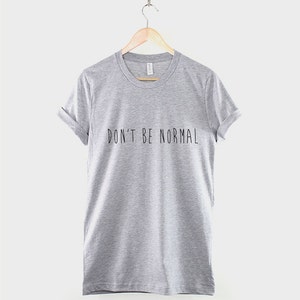 May include: A heather grey t-shirt with the text "DON'T BE NORMAL" printed in black.