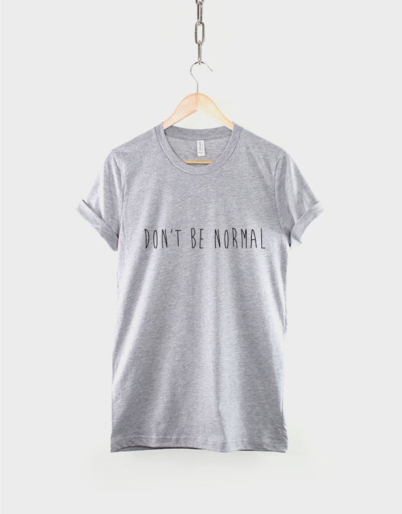 May include: A heather grey t-shirt with the text "DON'T BE NORMAL" printed in black.