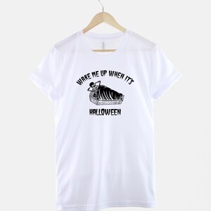 Puede incluir: Camiseta blanca con un gr&aacute;fico negro de un esqueleto en un ata&uacute;d con el texto "Despi&eacute;rtame cuando sea Halloween".