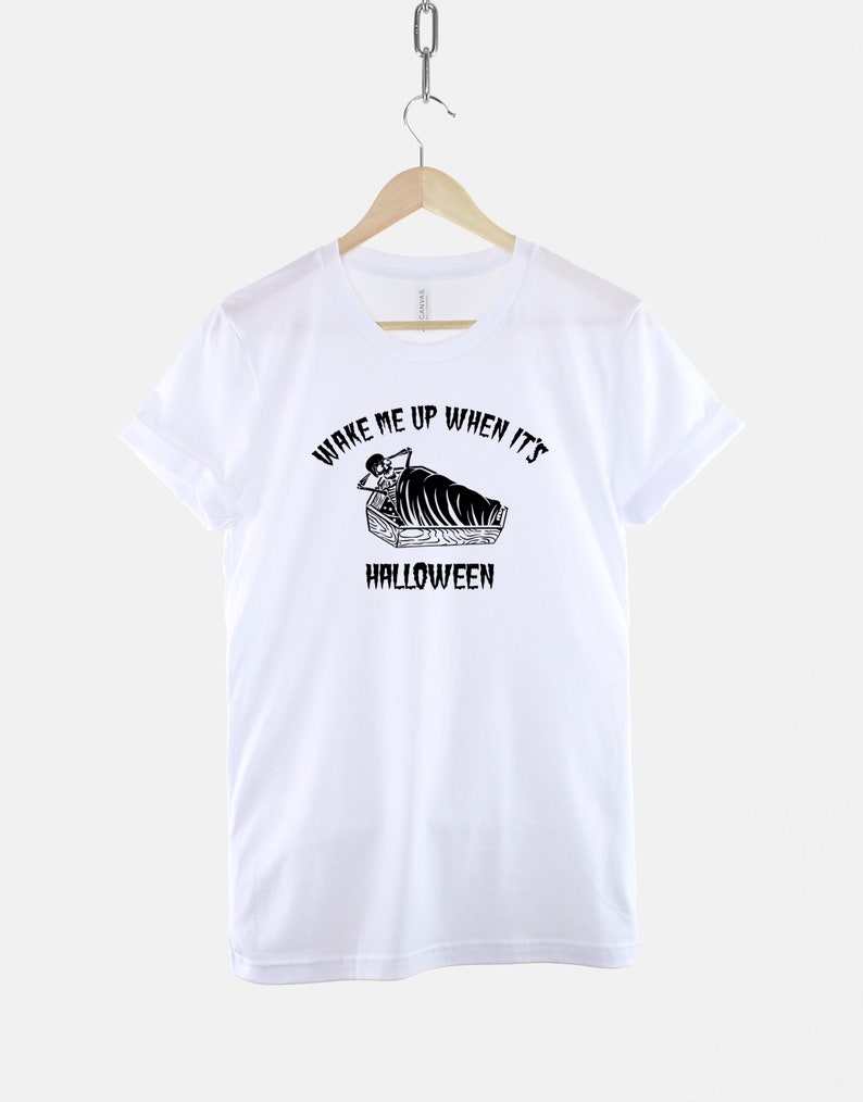 Puede incluir: Camiseta blanca con un gr&aacute;fico negro de un esqueleto en un ata&uacute;d con el texto "Despi&eacute;rtame cuando sea Halloween".