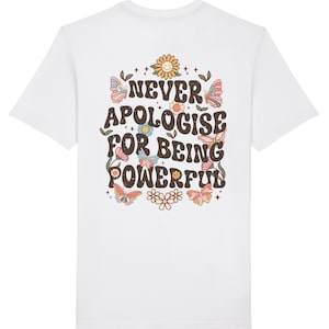 May include: White t-shirt with a graphic print of flowers, butterflies, and stars. The text "NEVER APOLOGISE FOR BEING POWERFUL" is printed in brown on the back of the shirt.