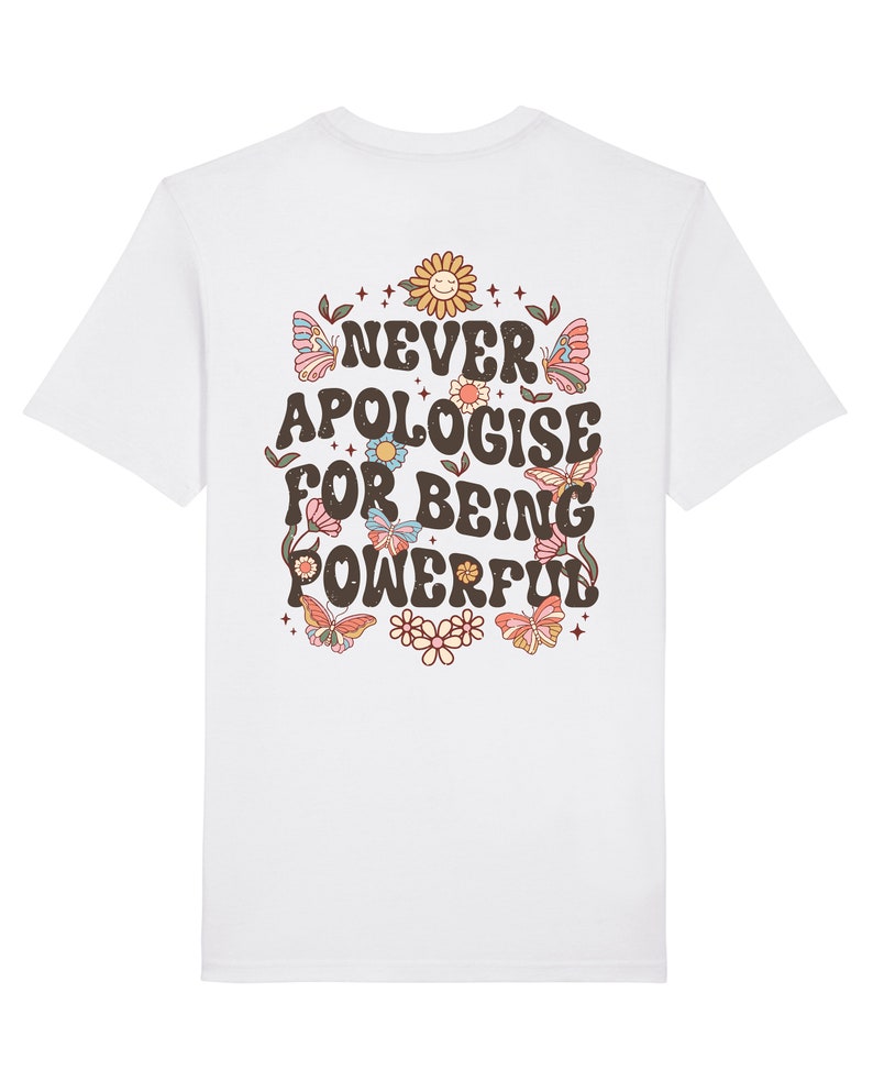 May include: White t-shirt with a graphic print of flowers, butterflies, and stars. The text "NEVER APOLOGISE FOR BEING POWERFUL" is printed in brown on the back of the shirt.