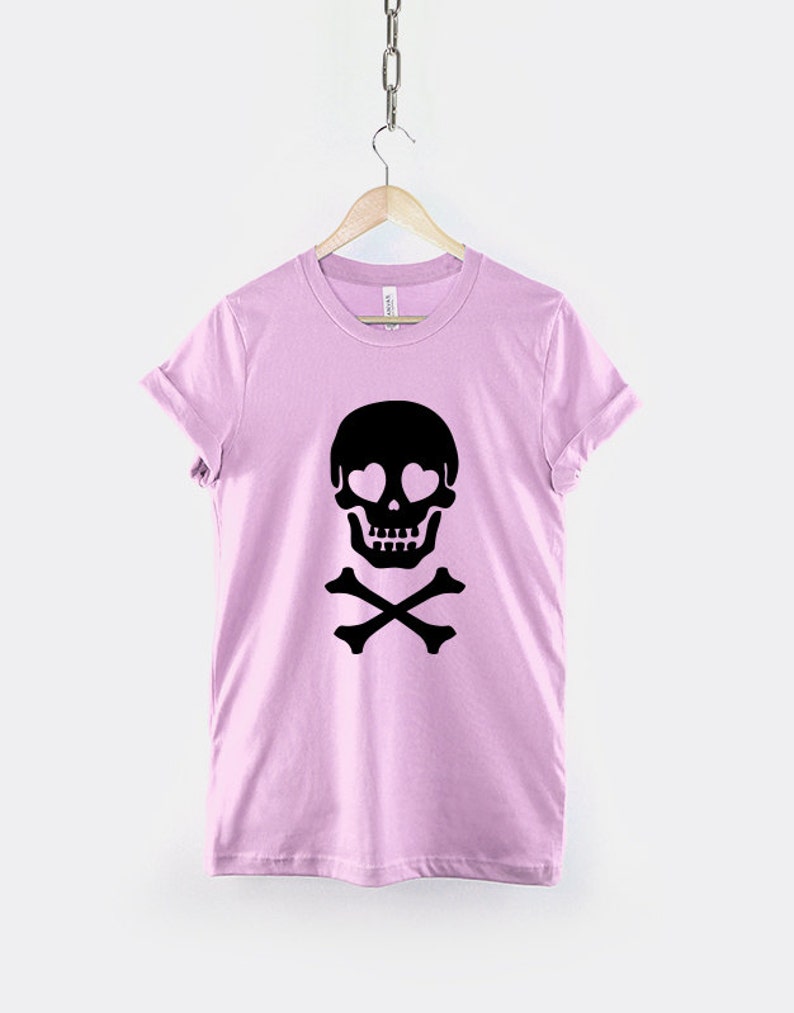 May include: A pink t-shirt with a black skull and crossbones design. The skull has hearts for eyes.