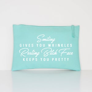 May include: A light turquoise zippered pouch with white text that reads "Smiling gives you wrinkles, Resting Bitch Face keeps you pretty." The pouch is rectangular and has a zipper closure.