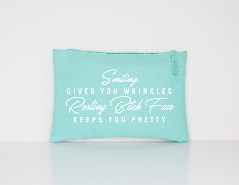May include: A light turquoise zippered pouch with white text that reads "Smiling gives you wrinkles, Resting Bitch Face keeps you pretty." The pouch is rectangular and has a zipper closure.