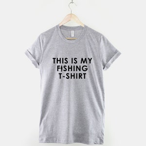Może przedstawiać: Szary t-shirt z nadrukiem "THIS IS MY FISHING T-SHIRT" w kolorze czarnym.