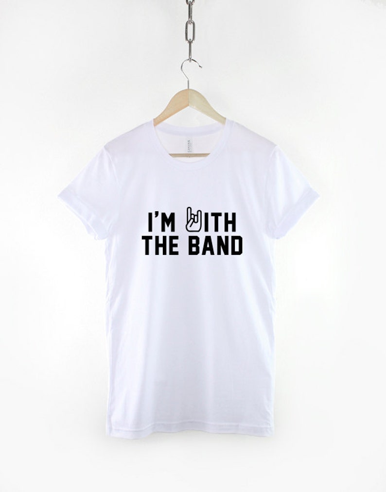 Puede incluir: Camiseta blanca con texto negro que dice "I'm with the band" y un gesto de mano rock and roll negro.