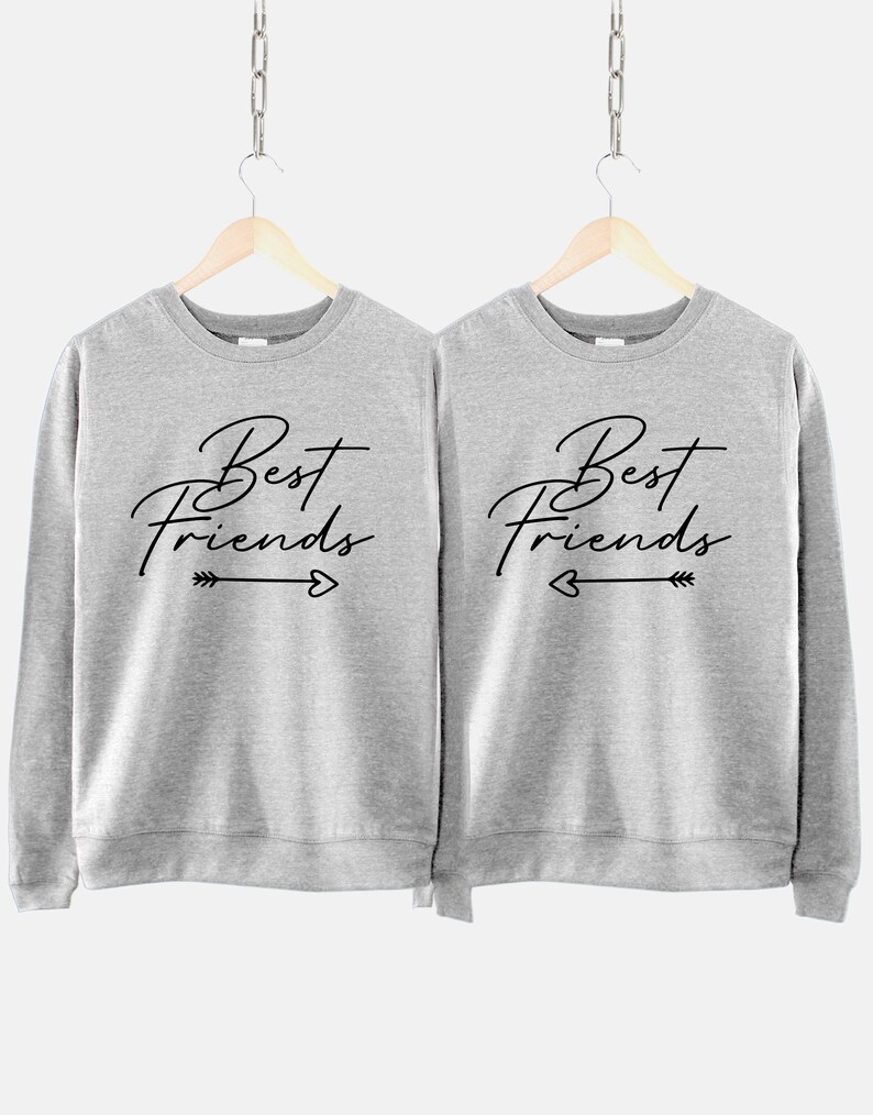 Może przedstawiać: Dwie szare bluzy z napisem "Best Friends" w czarnym kolorze z motywem strzałki i serca.