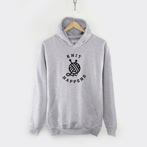 K&ouml;nnte beinhalten: Grauer Kapuzenpullover mit einem schwarzen Aufdruck einer Wollkn&auml;uel und Stricknadeln mit dem Text "Knit Happens".