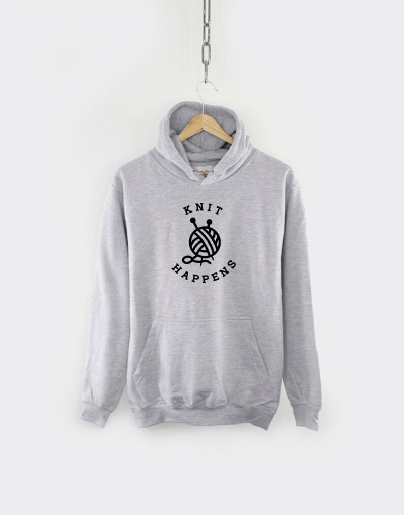 K&ouml;nnte beinhalten: Grauer Kapuzenpullover mit einem schwarzen Aufdruck einer Wollkn&auml;uel und Stricknadeln mit dem Text "Knit Happens".