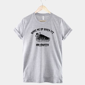 Puede incluir: Camiseta gris con un gr&aacute;fico negro de un esqueleto en un ata&uacute;d. El texto dice "Despi&eacute;rtame cuando sea Halloween".