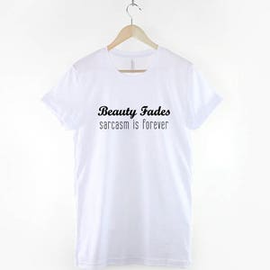 May include: White t-shirt with black text that reads "Beauty Fades sarcasm is forever".